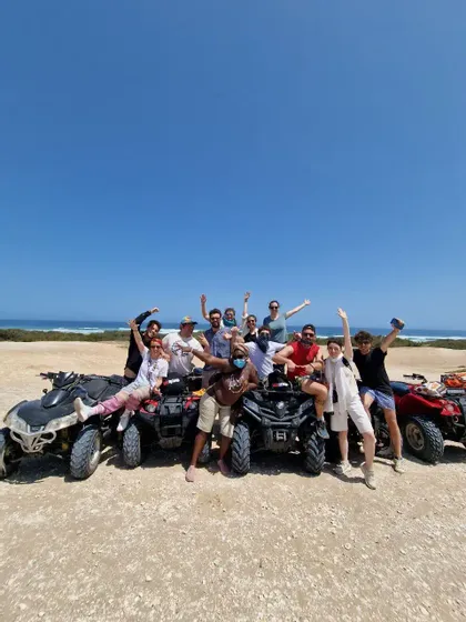 Eine WeRoad-Gruppe macht ein Foto mit ihren Quads auf einem Feldweg vor der Kulisse des Meeres.