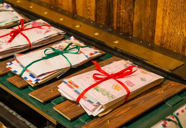 Bündel von Kinder-Weihnachtsbriefen, mit roten und grünen Bändern verschnürt, sind auf einem hölzernen Sortierband angeordnet.