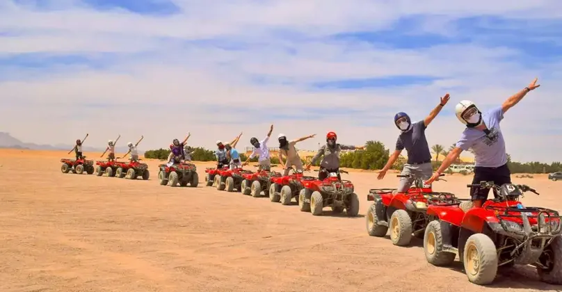 Un viaggio di gruppo WeRoad con le braccia aperte in posa su una fila di quad rossi in un paesaggio desertico.