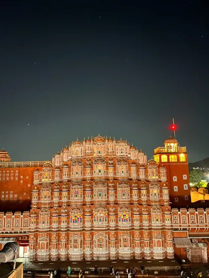 Un palazzo rosa ornato con molte finestre dal design intricato, illuminato di notte sotto un cielo scuro e stellato.