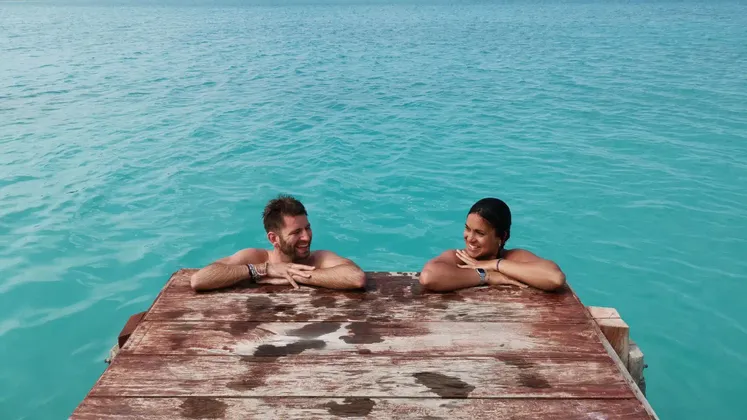 Un uomo e una donna in un viaggio di gruppo WeRoad si appoggiano a un molo di legno, sorridendosi a vicenda nell'acqua turchese.