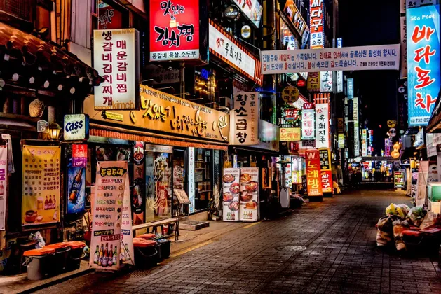 Eine enge Stadtgasse bei Nacht, gesäumt von Restaurants und hell erleuchtet von zahlreichen farbigen Neonschildern mit koreanischen Schriftzeichen.