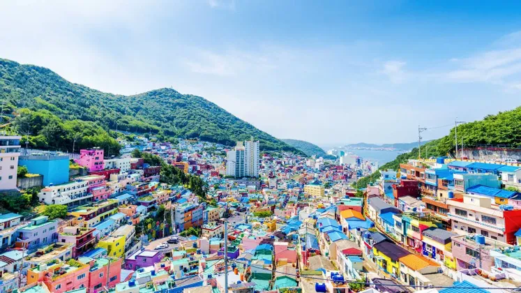 Une vue panoramique d'un village aux bâtiments aux couleurs vives s'étageant le long d'un flanc de montagne verdoyant jusqu'à la mer.