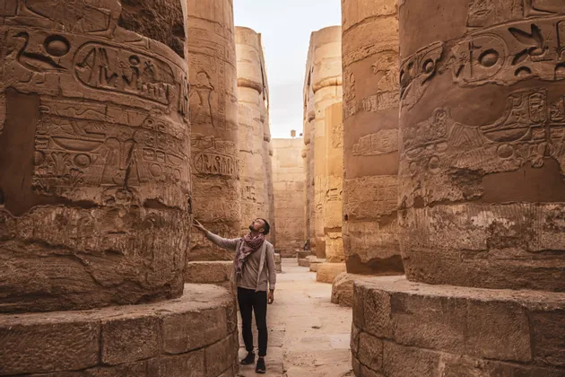 Ein Mann steht in einer alten Tempelhalle und blickt zu den Hieroglyphen auf, die in die massiven Steinsäulen gemeißelt sind.