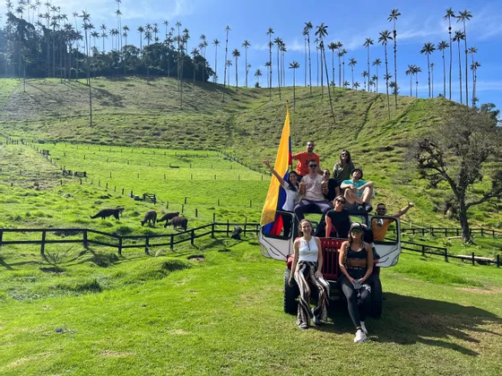 Eine WeRoad Gruppenreise mit einer kolumbianischen Flagge posiert auf einem Geländewagen in einem Tal mit hohen Palmen.