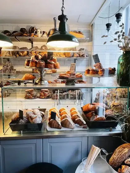 La vitrine d'une boulangerie, remplie de divers croissants et pâtisseries sous des lumières suspendues chaleureuses.