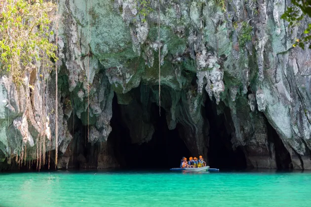 Eine WeRoad Gruppenreise in einem kleinen Boot am Eingang einer großen Meereshöhle mit türkisfarbenem Wasser.