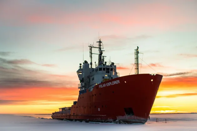 La rompighiaccio rossa Polar Explorer giace su una vasta distesa di mare ghiacciato sotto un cielo al tramonto dai colori vivaci.