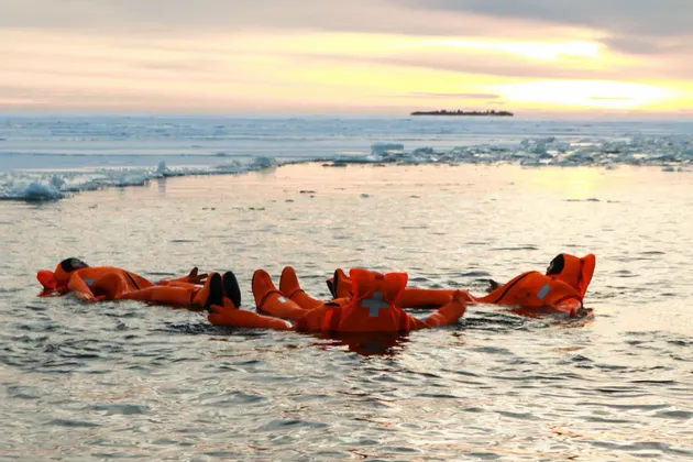 Un viaggio di gruppo WeRoad con tute di immersione arancioni, che galleggia sulla schiena in acqua ghiacciata al tramonto.