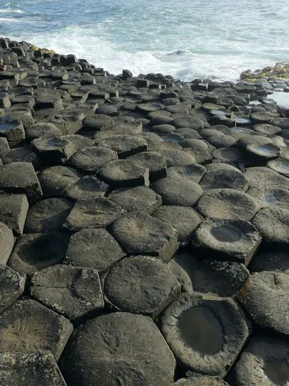 Colonne esagonali di basalto si incastrano a formare una pavimentazione naturale che incontra il mare agitato, con onde dalle creste bianche.