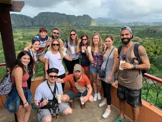 Un gruppo WeRoad in posa per una foto con bevande su un punto panoramico che si affaccia su una lussureggiante valle verde e le montagne.