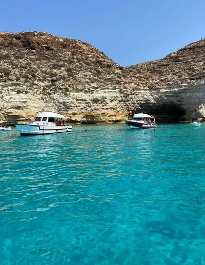 Un viaggio di gruppo WeRoad su due barche ancorate in una caletta con acqua turchese, accanto a una parete rocciosa.
