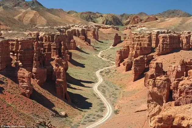 Vista dall'alto di una strada sterrata tortuosa che attraversa un canyon profondo con formazioni rocciose rosse e vegetazione verde.