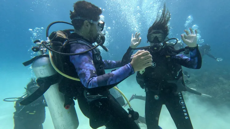 Due persone in un viaggio di gruppo WeRoad interagiscono mentre fanno immersioni subacquee, con altri subacquei sullo sfondo.