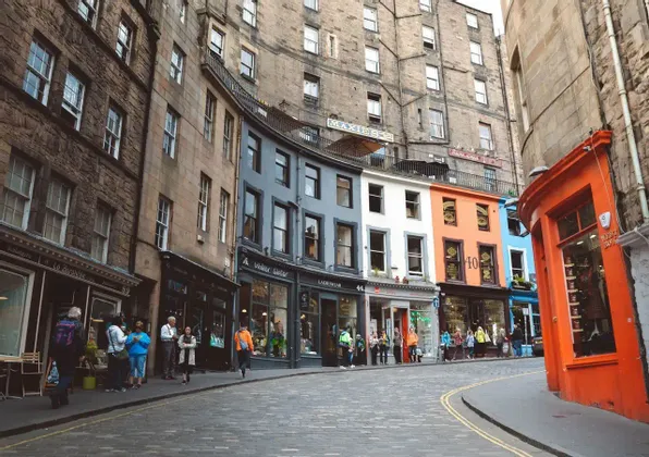 Una calle adoquinada y curva está flanqueada por coloridos edificios históricos y tiendas, con peatones en la acera.