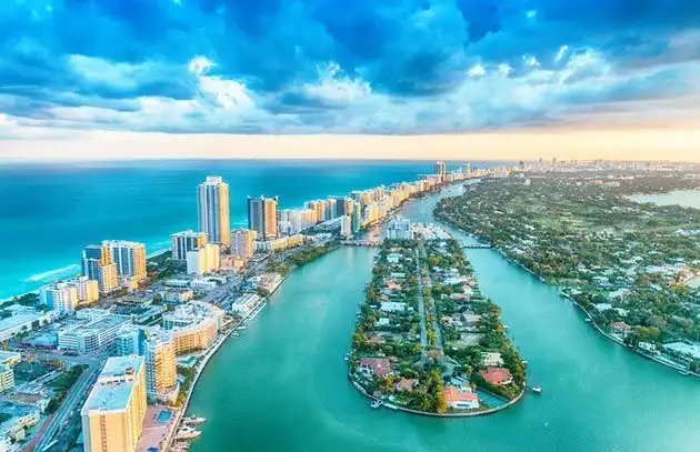 Vista aerea di una città costiera con grattacieli lungo la spiaggia e un corso d'acqua che separa isole residenziali.