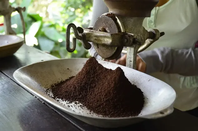 Un macinacaffè manuale d'epoca che eroga caffè macinato fresco in un piattino bianco su un tavolo di legno.