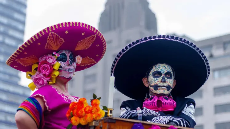 Due persone in costumi tradizionali e sombreri con i volti dipinti come teschi calavera per una festa.