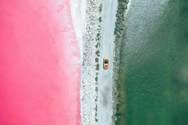 Una vista aerea di un'auto gialla che guida su una strada che separa un lago rosa vibrante da uno verde scuro.