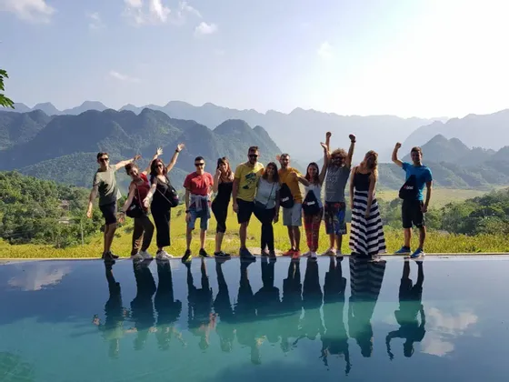 Eine WeRoad-Gruppe posiert am Rande eines Infinity-Pools, mit ihren Spiegelungen im Wasser und Bergen im Hintergrund.