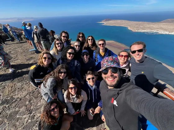 Un gruppo WeRoad si scatta un selfie da un punto panoramico elevato, con l'oceano blu e un'isola sullo sfondo.