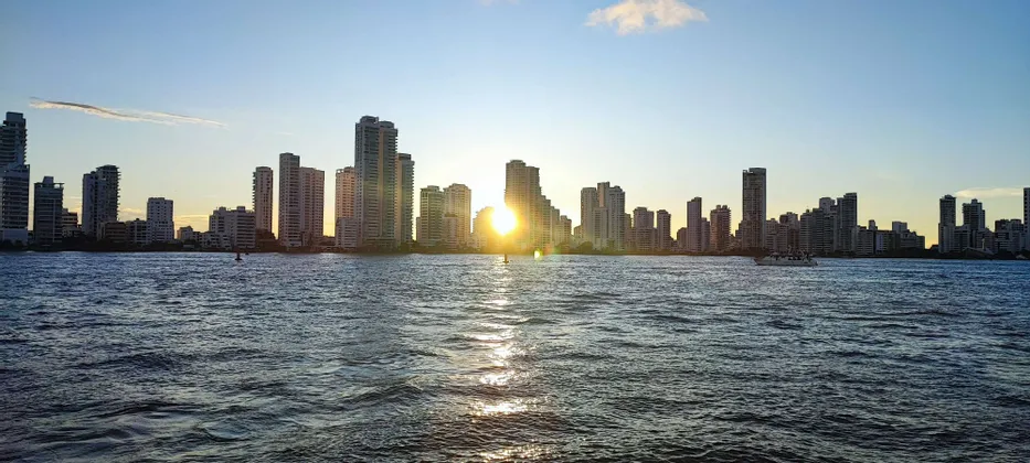 Eine Skyline hoher Gebäude, vom Wasser aus bei Sonnenuntergang gesehen, mit der Spiegelung der Sonne auf den Wellen.