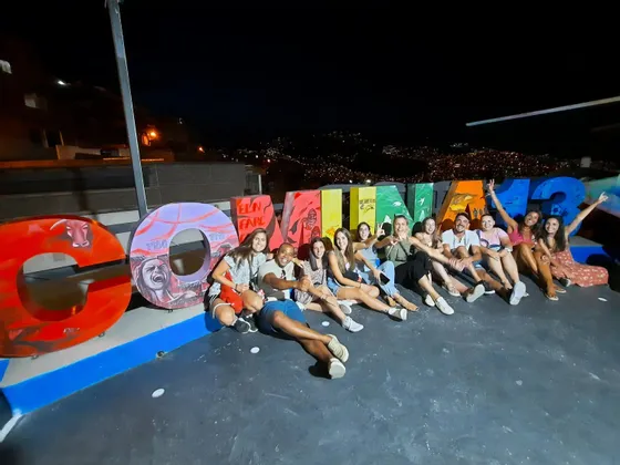 Eine WeRoad-Reisegruppe posiert nachts auf einem Dach für ein Foto, sitzend vor großen, bunten Graffiti-Buchstaben.