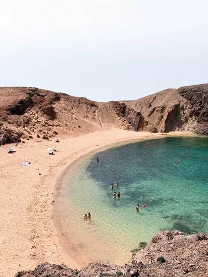 Menschen schwimmen im klaren türkisfarbenen Wasser einer abgelegenen Bucht mit Sandstrand und felsigen Klippen.