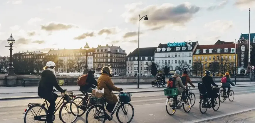 Un grupo WeRoad pasea en bicicleta por una calle de la ciudad con edificios antiguos al atardecer.