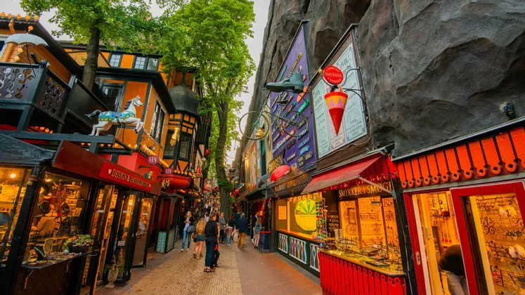 Personas paseando por una calle estrecha y pintoresca, con edificios coloridos y decorados y tiendas luminosas.