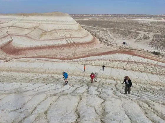 Un viaggio di gruppo WeRoad cammina su terra bianca screpolata di fronte a grandi colline a strisce colorate sotto un cielo ampio.