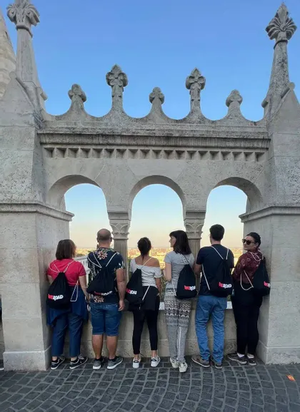 Un viaggio di gruppo WeRoad visto da dietro, in piedi su un balcone di pietra con archi e con vista su un paesaggio urbano.