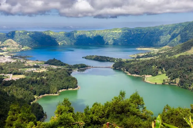 Veduta aerea di due laghi vulcanici, uno blu e uno verde, separati da un ponte e circondati da lussureggianti montagne verdi.