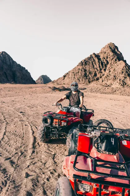 Una persona in un viaggio di gruppo WeRoad cavalca un quad rosso nel deserto con montagne rocciose sullo sfondo.
