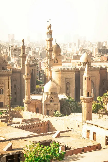 Un complesso storico di moschee in pietra con cupole e minareti che domina un paesaggio urbano denso sotto un cielo luminoso e velato.