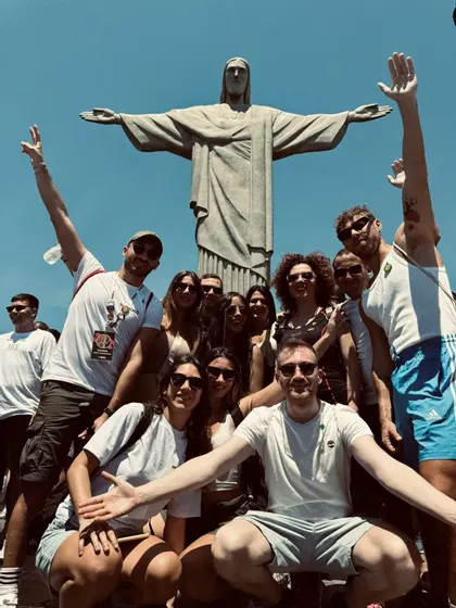 Un gruppo WeRoad in viaggio posa per una foto di gruppo davanti alla statua del Cristo Redentore sotto un cielo sereno.