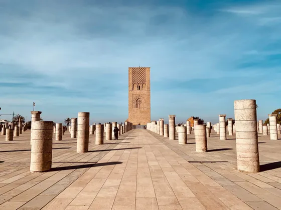 Reihen von Steinsäulen füllen einen weiten, gepflasterten Platz, der zu einem hohen, historischen Turm unter blauem Himmel führt.