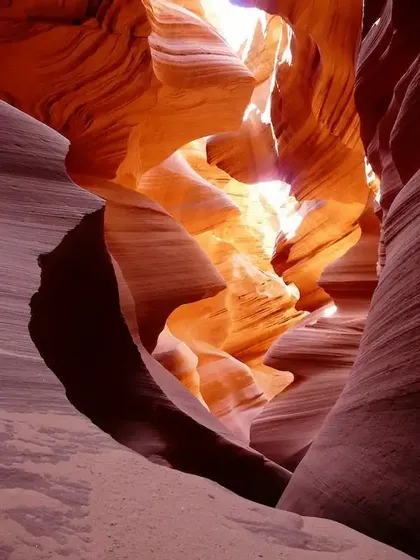 La luce del sole si riversa in uno stretto canyon a fessura, mettendo in risalto la trama ondulata delle pareti di arenaria arancione e rossa.