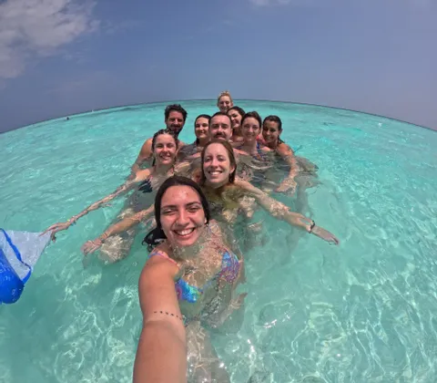 Un gruppo WeRoad si scatta un selfie sorridente mentre nuota in acque oceaniche limpide e turchesi.