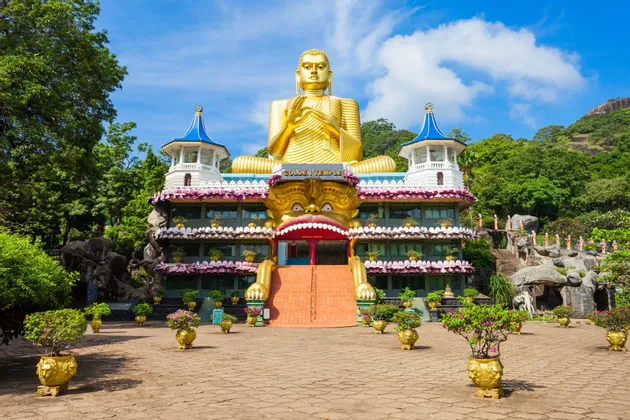 Una gigantesca statua dorata di Buddha si erge in cima all'ornato edificio del Tempio d'Oro, con scale che conducono a un grande ingresso a bocca di mostro.